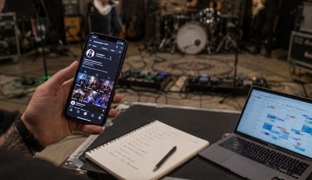 Bandmitglied plant Social-Media-Beiträge am Smartphone im Proberaum, während die Band im Hintergrund probt.