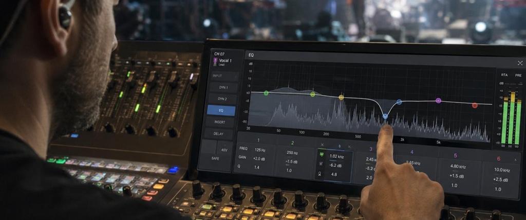 Tontechniker bedient bei einem Live-Konzert ein digitales Mischpult mit sichtbarer EQ-Kurve auf dem Display.