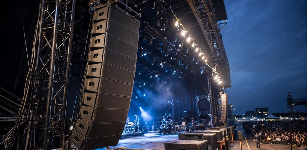 Geflogenes Line-Array mit mehreren Lautsprechermodulen an einer beleuchteten Open-Air-Konzertbühne bei Nacht.