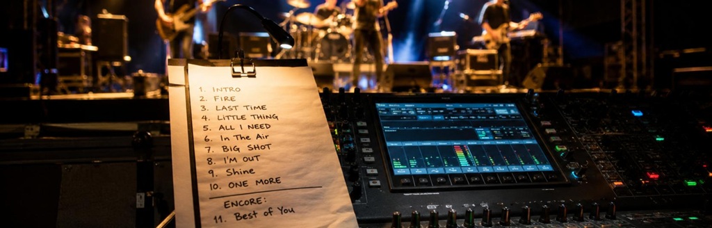 Setliste für Auftritt erstellen: handgeschriebene Songliste auf FOH-Mischpult vor Live-Band mit Bühne, Lichttechnik und Veranstaltungstechnik.