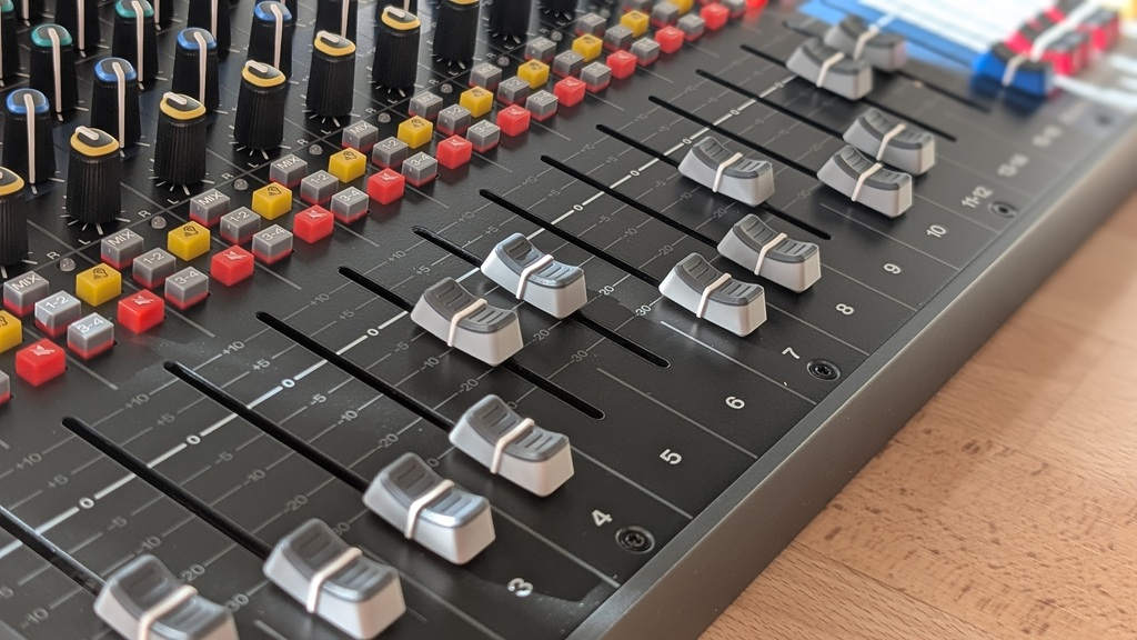 Detailaufnahme der Kanalfader des Soundcraft Signature Plus 16 mit Pegelskalen sowie farbigen Routing- und Mute-Tasten.